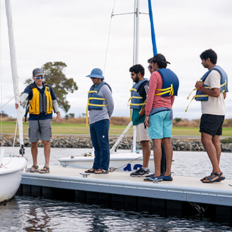 students receiving sailing instructions at shoreline lake.