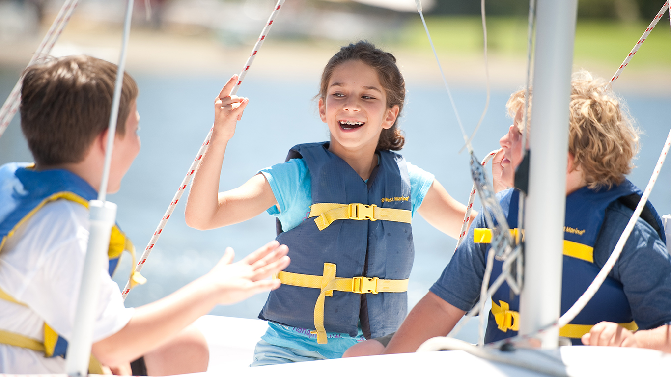 A girl smiling in a sailboat with two boys.