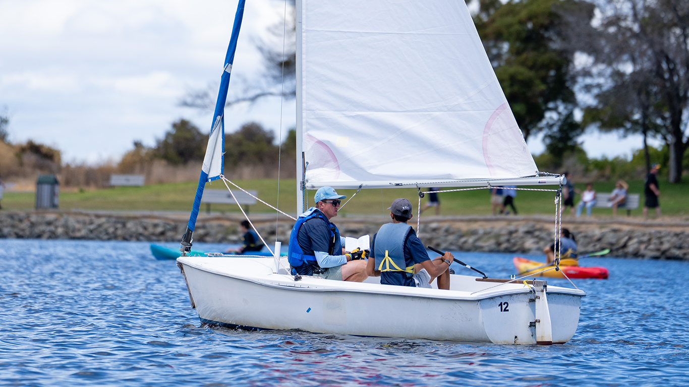 A sailing instructor teaching a young peron how to sail on shoreline lake