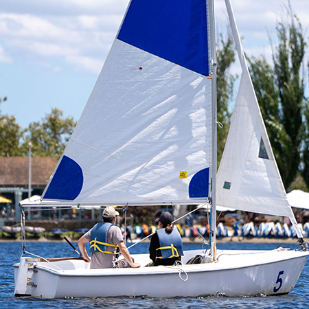 A man and woman sailing a boat on shoreline lake.