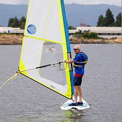 An older man on a windsurfer in the lake.