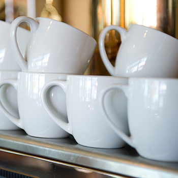 A bunch of white coffee cups stacked on top of an espresso machine