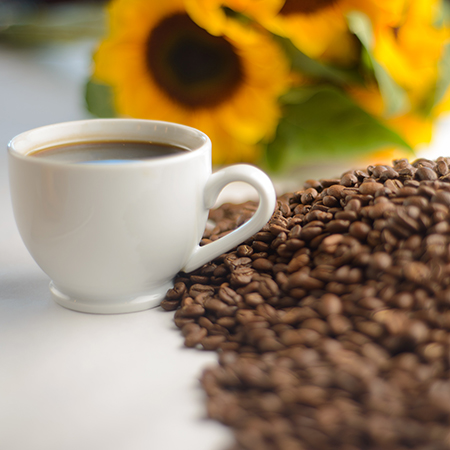 A cup of coffee sitting next to a large pile of coffee beans.