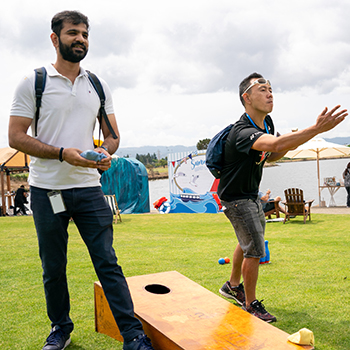 Two men playing a game of cornhole at shoreline lake.